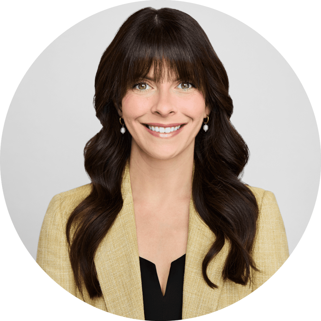 A professional headshot of Leeann Dastous, smiling warmly. She is wearing a beige blazer, a black top, and pearl earrings, with her dark brown hair styled in soft waves. The background is plain and neutral.